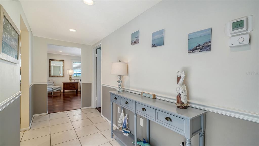 A hallway features a gray console table, coastal decor, and tile flooring leading to another room — 2721 RIVERBLUFF PLACE UNIT V-50, SARASOTA, FL