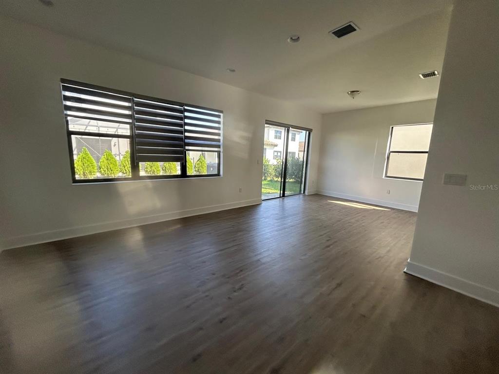 An empty living room with wood-look flooring, large windows, and sliding glass doors — 5525 AGOSTINO WAY, AVE MARIA, FL