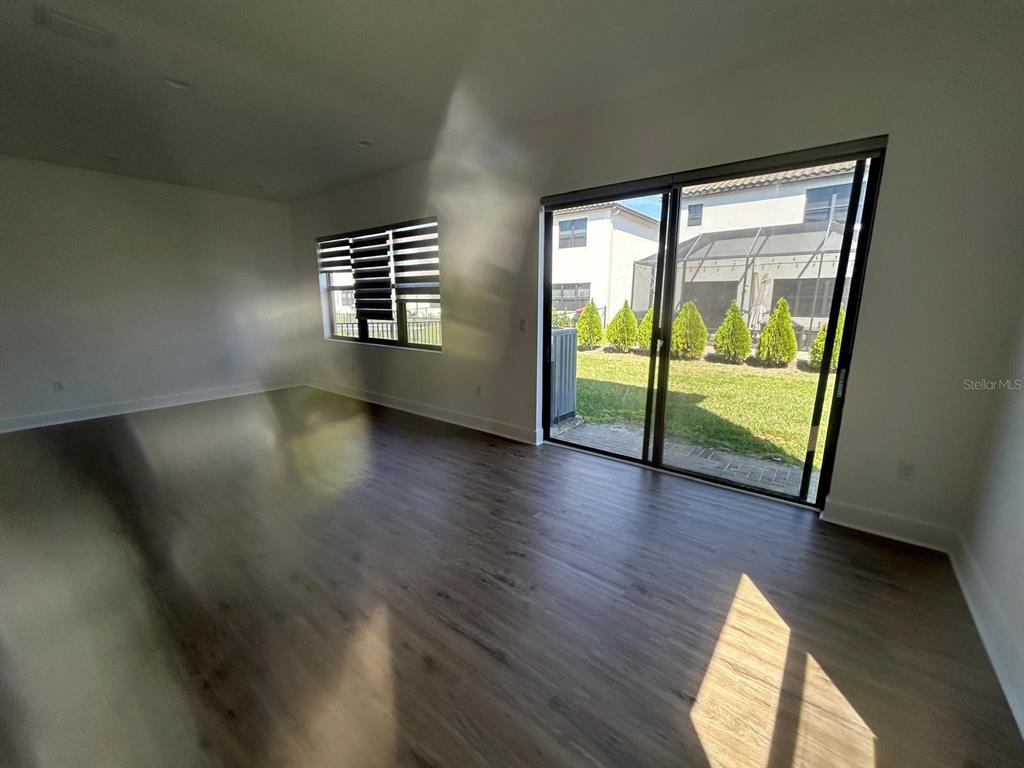 An empty room features wood-look flooring, a large window, and sliding glass doors to a yard — 5525 AGOSTINO WAY, AVE MARIA, FL