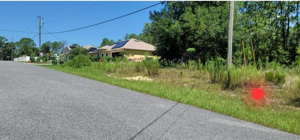 A vacant, grassy residential lot sits next to a paved road with houses in the background — 7163 N GLENRIDGE CIRCLE, CITRUS SPRINGS, FL