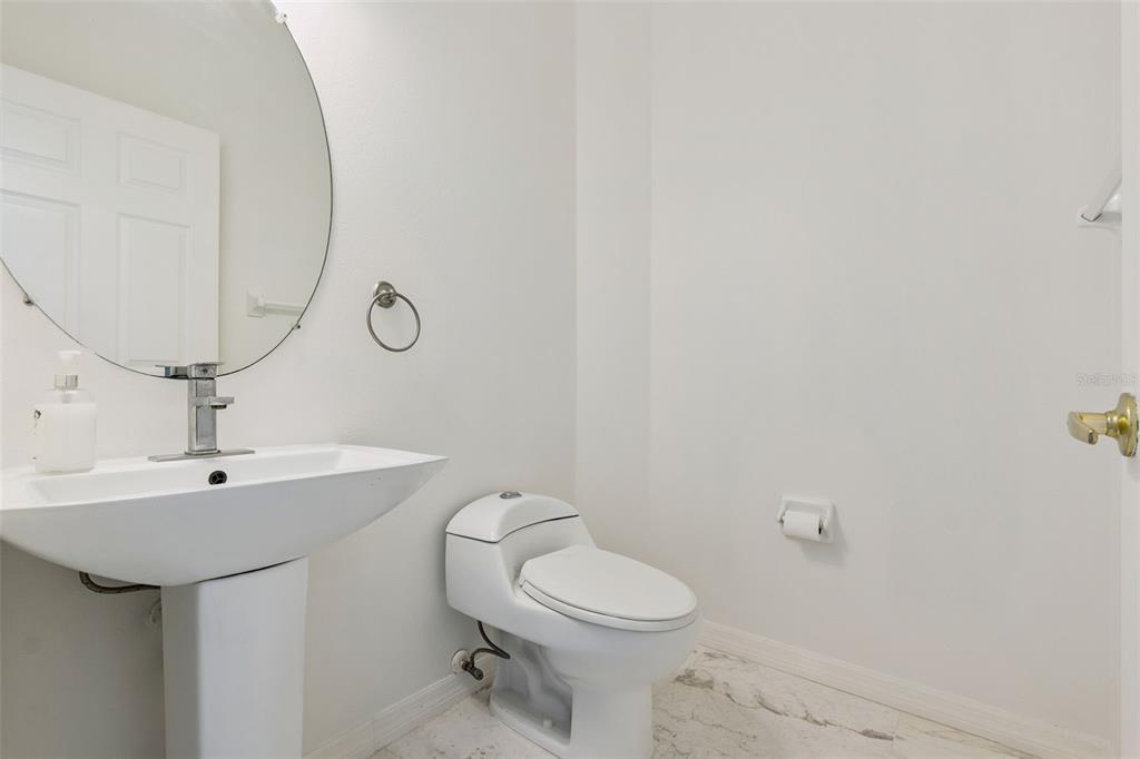 A small bathroom features a pedestal sink, a round mirror, and a white toilet — 571 MASALO PLACE, LAKE MARY, FL