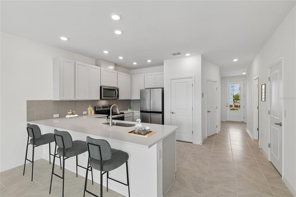 A modern kitchen features white cabinetry, stainless steel appliances, a quartz island, and bar stools — 6406 JENSEN VIEW AVENUE, APOLLO BEACH, FL