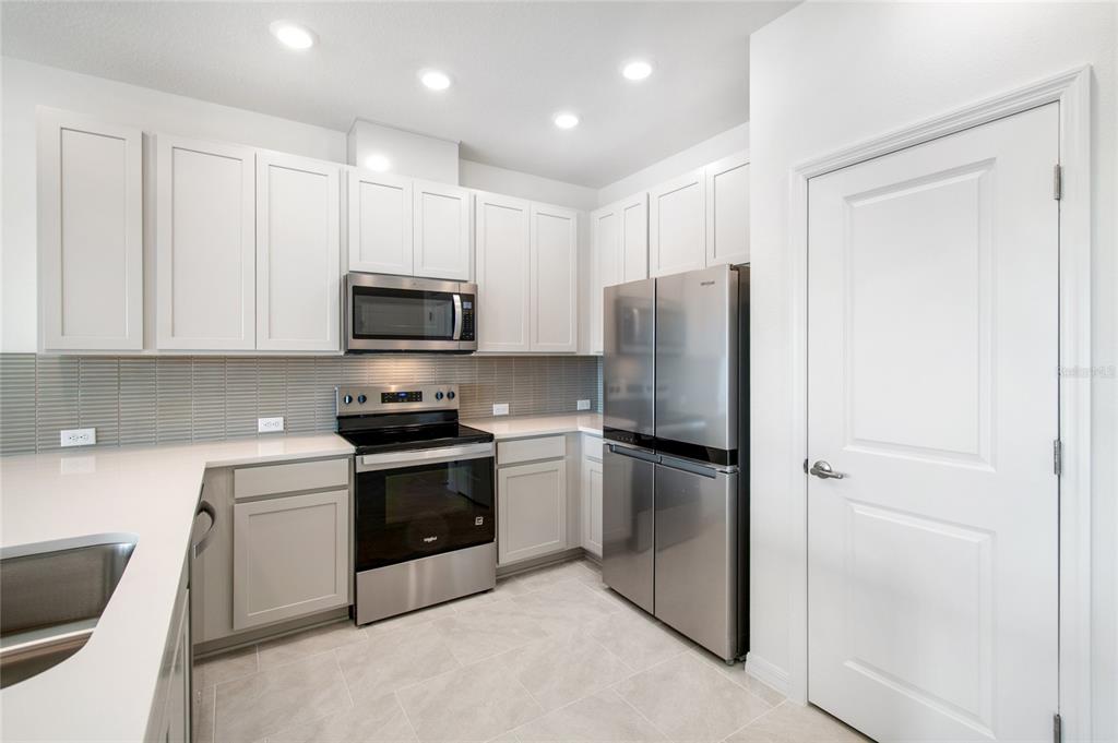 A modern kitchen features white cabinets, stainless steel appliances, light countertops, and gray tile flooring — 6406 JENSEN VIEW AVENUE, APOLLO BEACH, FL