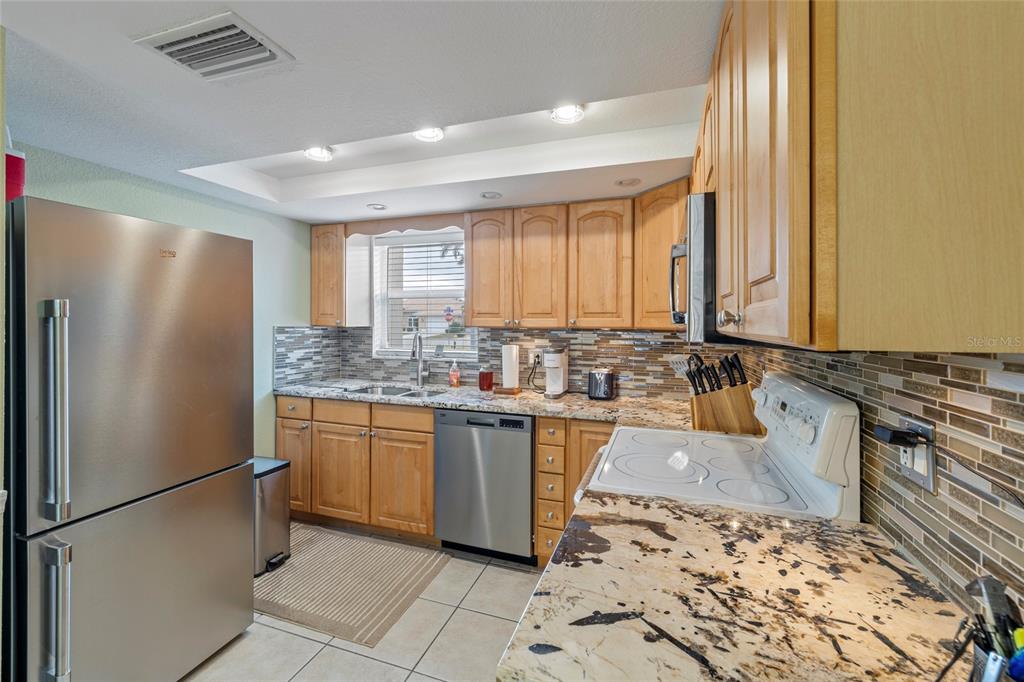 A kitchen with light wood cabinets, granite countertops, stainless steel appliances, and a tiled backsplash — 311 GARVIN STREET UNIT 411B, PUNTA GORDA, FL