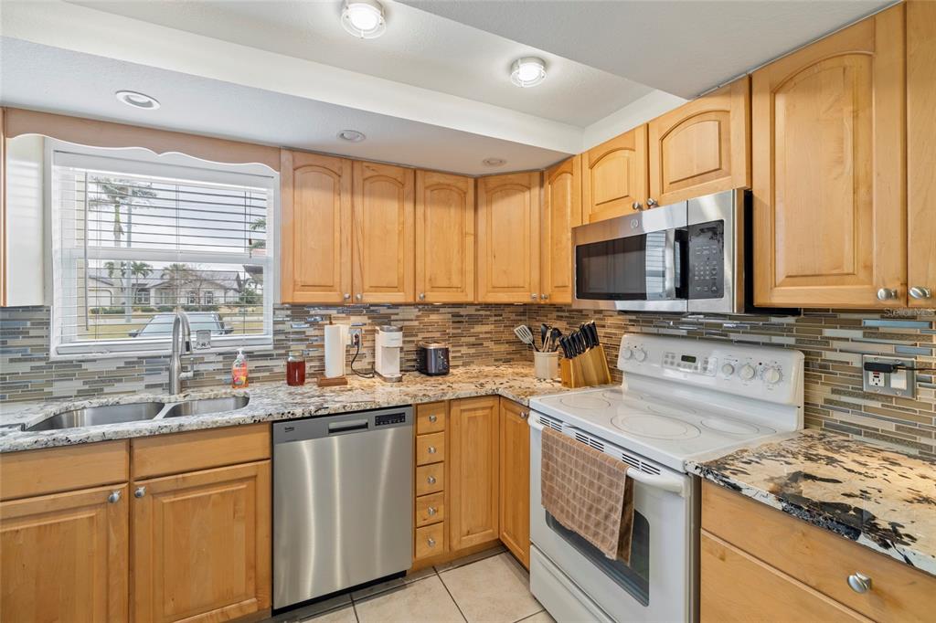 A kitchen with light wood cabinets, granite countertops, stainless steel appliances, and a tiled backsplash — 311 GARVIN STREET UNIT 411B, PUNTA GORDA, FL