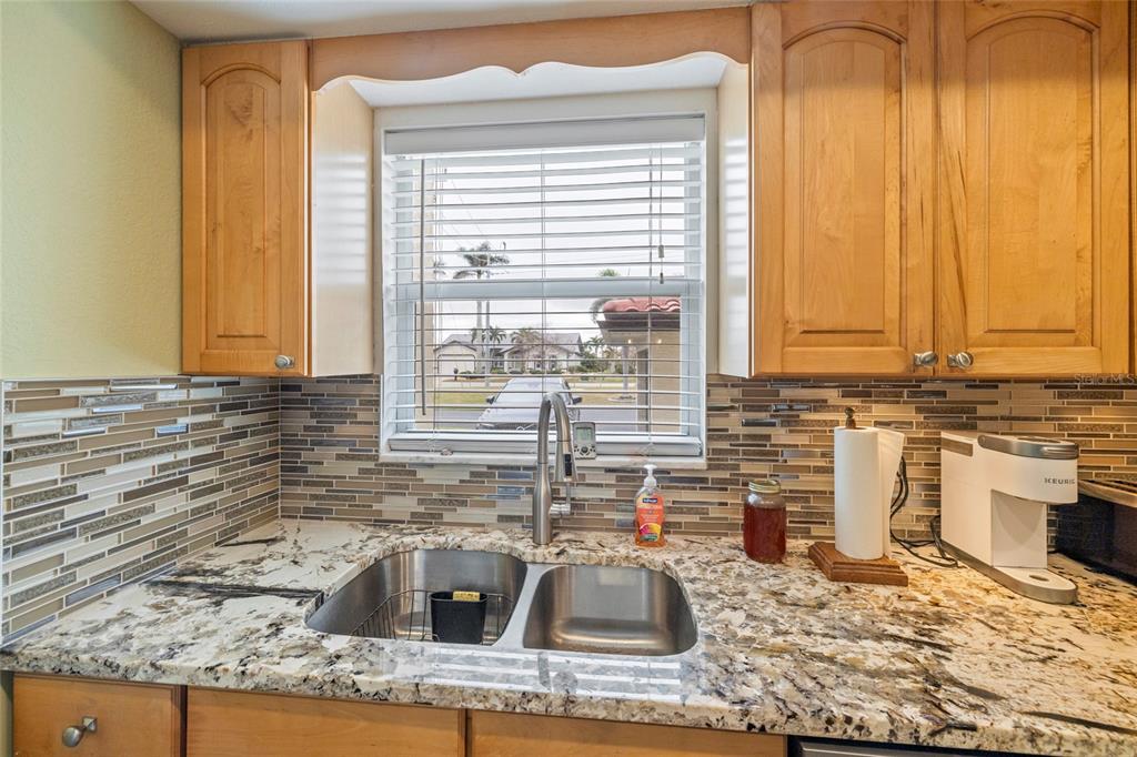 A kitchen sink area features granite countertops, a mosaic tile backsplash, and light wood cabinets — 311 GARVIN STREET UNIT 411B, PUNTA GORDA, FL