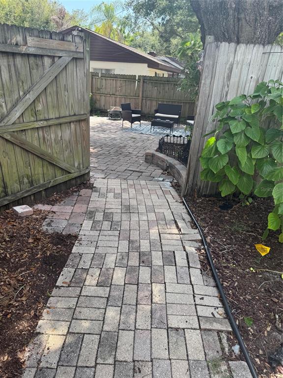 A brick walkway leads through a wooden gate to a paved patio with outdoor furniture — 6408 N HIGHLAND AVENUE, TAMPA, FL