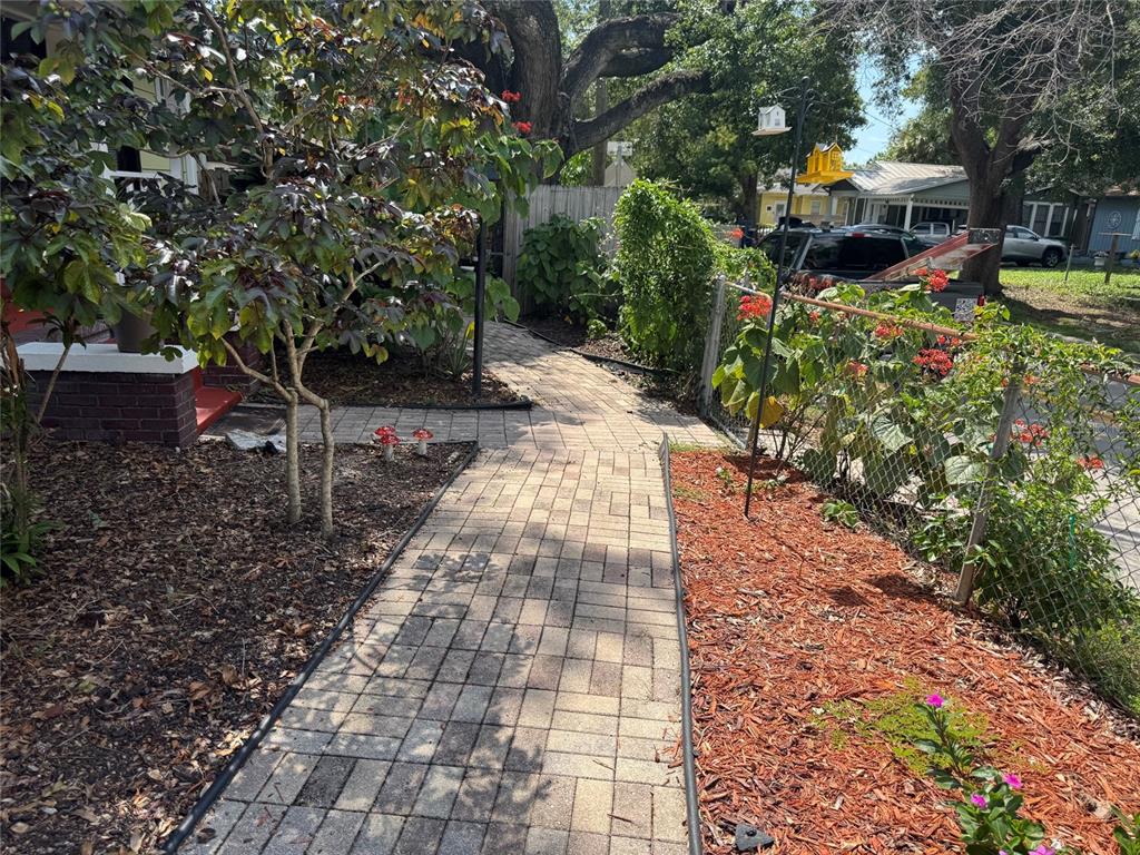 A brick paver walkway leads through a front yard with mulch beds and a chain-link fence — 6408 N HIGHLAND AVENUE, TAMPA, FL
