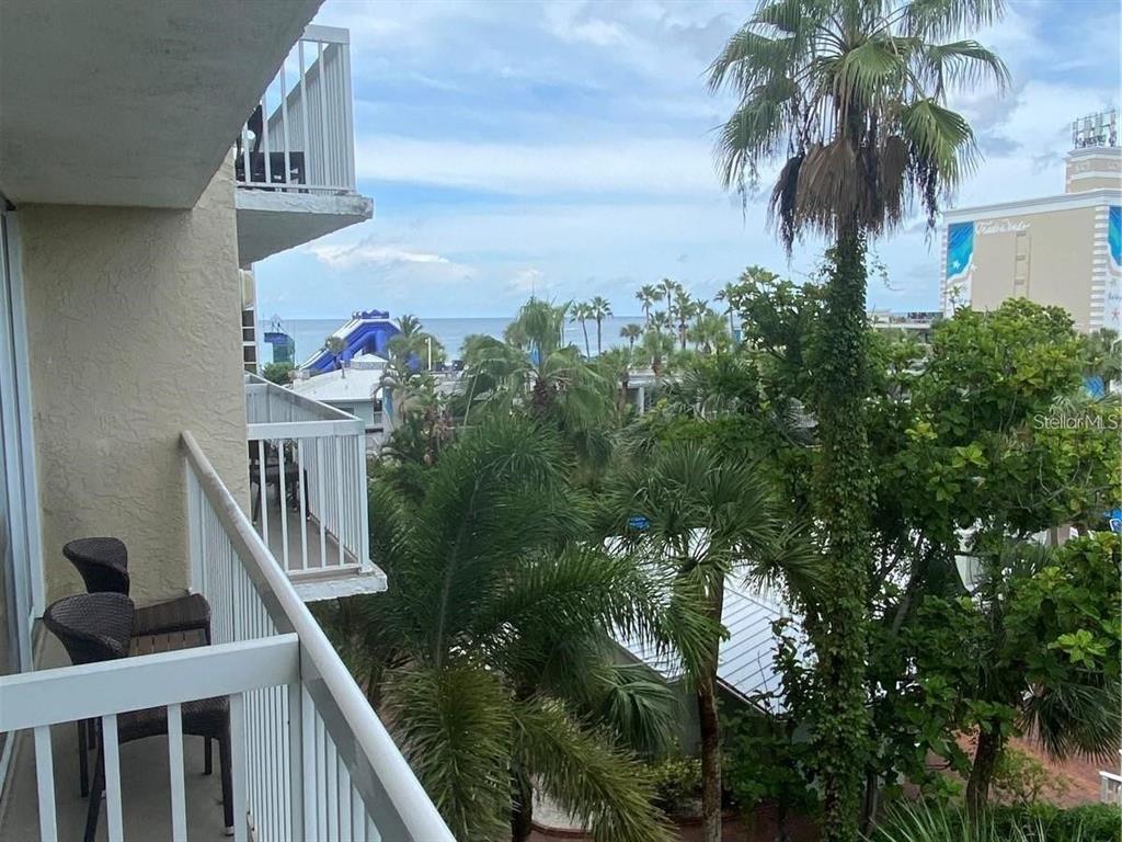 A balcony view overlooks tropical trees, a blue water slide, and the distant ocean — 5500 GULF BOULEVARD UNIT 4246, ST PETE BEACH, FL