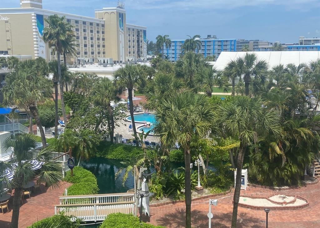 An elevated view of a resort courtyard featuring a swimming pool, pond, and palm trees — 5500 GULF BOULEVARD UNIT 4246, ST PETE BEACH, FL