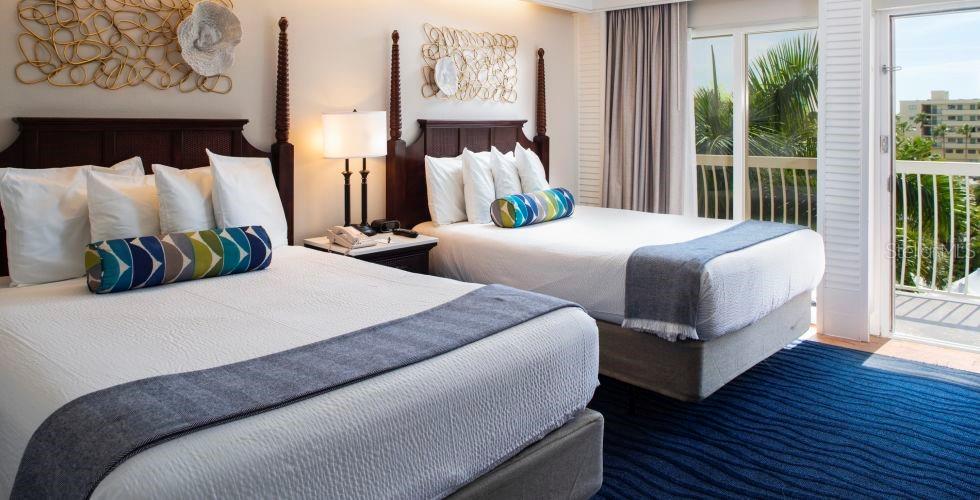 A hotel room features two queen beds, dark wood headboards, and a balcony with palm trees — 5500 GULF BOULEVARD UNIT 4246, ST PETE BEACH, FL