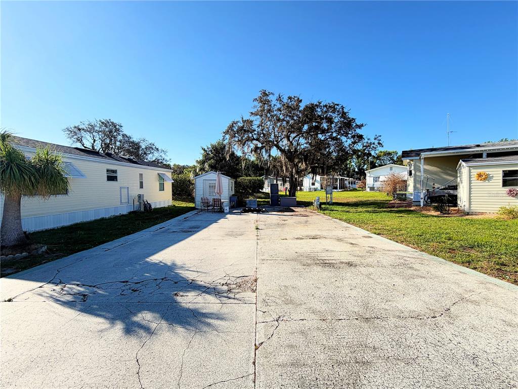 A wide concrete driveway sits between two mobile homes under a clear blue sky — 7350 MIDWAY LANE UNIT 54, LAKE WALES, FL