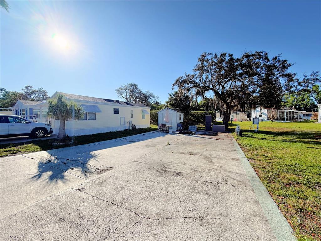 A concrete driveway sits between two mobile homes with a small shed in the background — 7350 MIDWAY LANE UNIT 54, LAKE WALES, FL