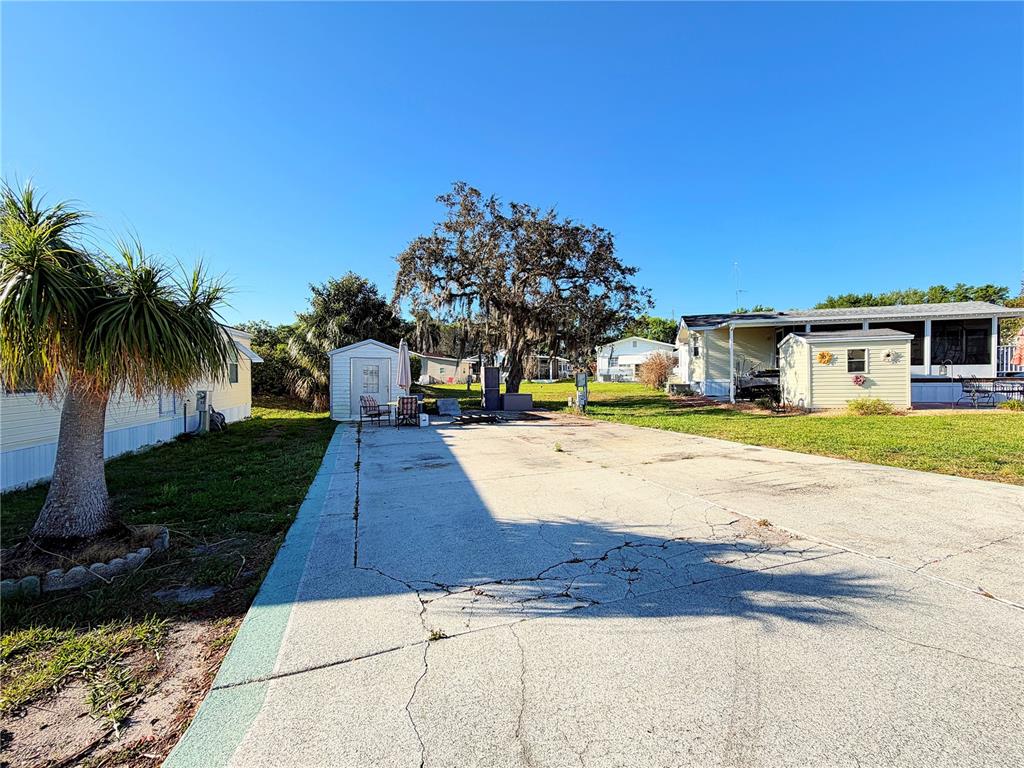 A concrete driveway leads to a light-colored mobile home with a shed and large tree — 7350 MIDWAY LANE UNIT 54, LAKE WALES, FL