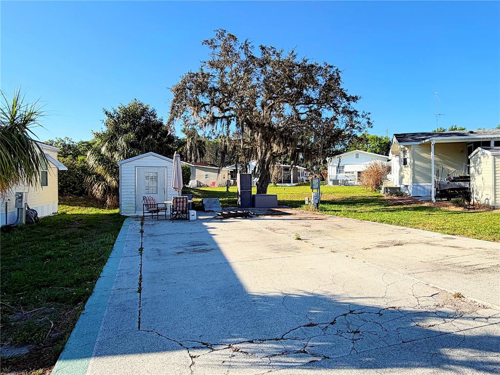 A concrete driveway leads to a small shed and a large tree in a yard — 7350 MIDWAY LANE UNIT 54, LAKE WALES, FL