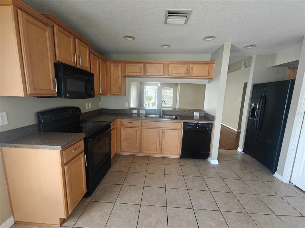 A kitchen with light wood cabinets, black appliances, dark countertops, and beige tile flooring — 8225 SUMMER WOOD LANE, RIVERVIEW, FL