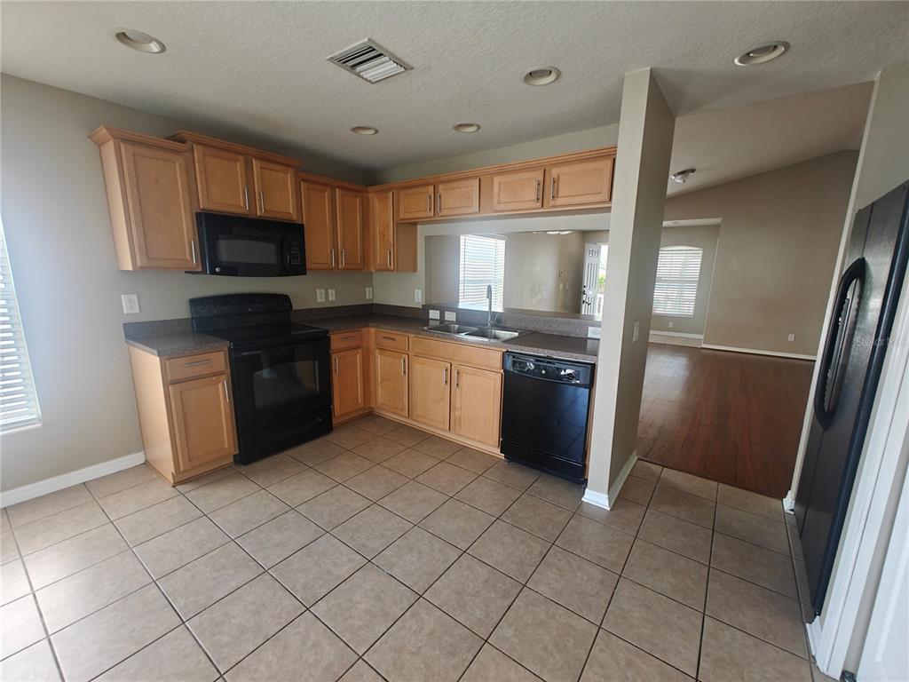 A kitchen features light wood cabinets, black appliances, dark countertops, and beige tile flooring — 8225 SUMMER WOOD LANE, RIVERVIEW, FL