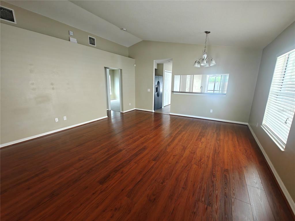 An empty living room features dark wood flooring, beige walls, and a vaulted ceiling — 8225 SUMMER WOOD LANE, RIVERVIEW, FL