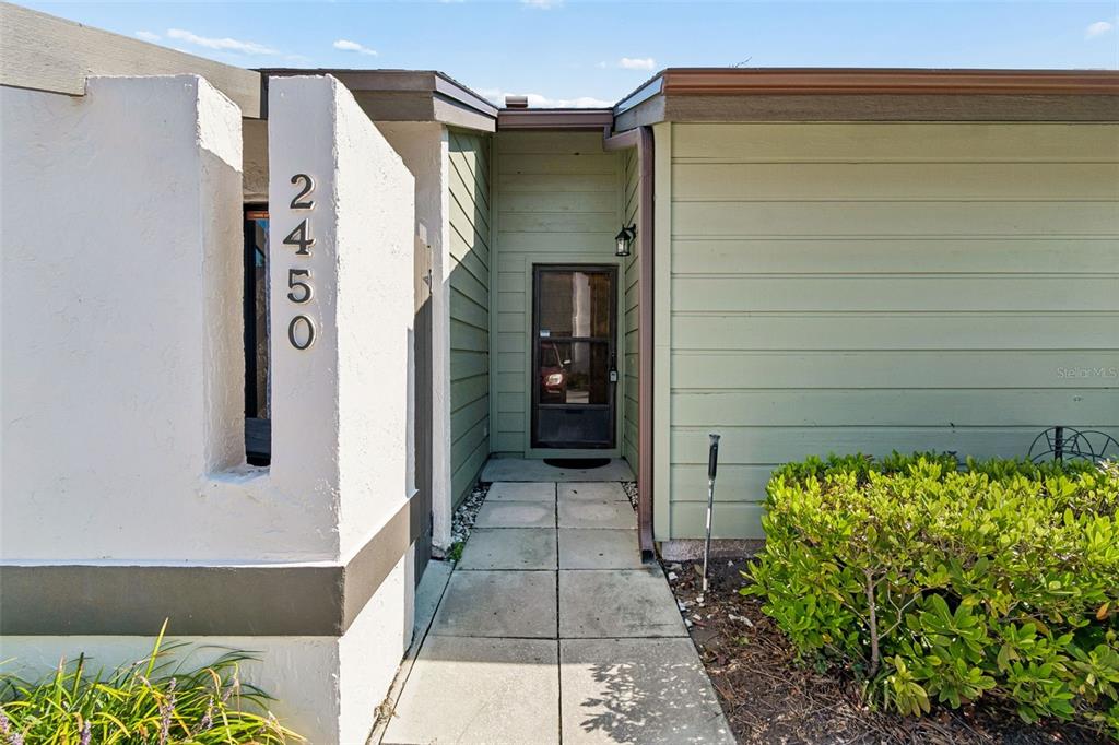 A concrete walkway leads to the front entrance of a house with light green siding — 2450 GRAND TETON CIRCLE UNIT 2450, WINTER PARK, FL