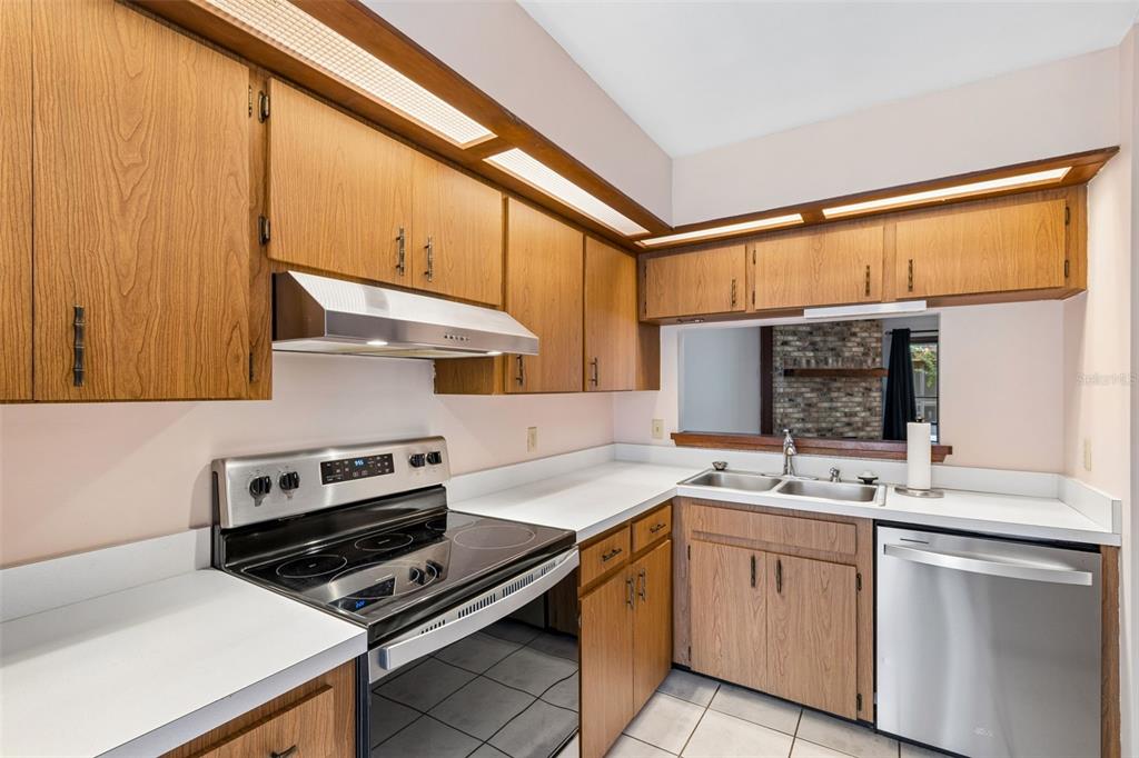 A kitchen with wood cabinets, white countertops, stainless steel appliances, and a pass-through window — 2450 GRAND TETON CIRCLE UNIT 2450, WINTER PARK, FL