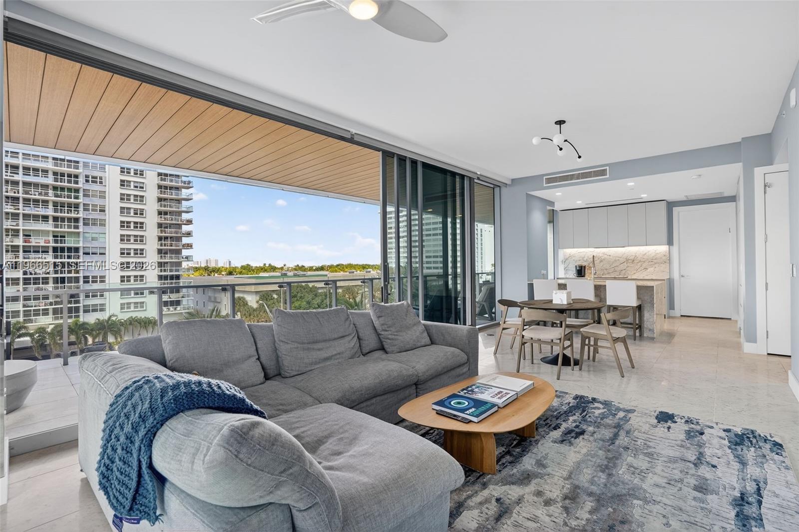 A modern living room with a gray sectional sofa, dining area, and a large balcony view — 5775 Collins Ave # 506, Miami Beach FL 33140, MIAMI BEACH, FL