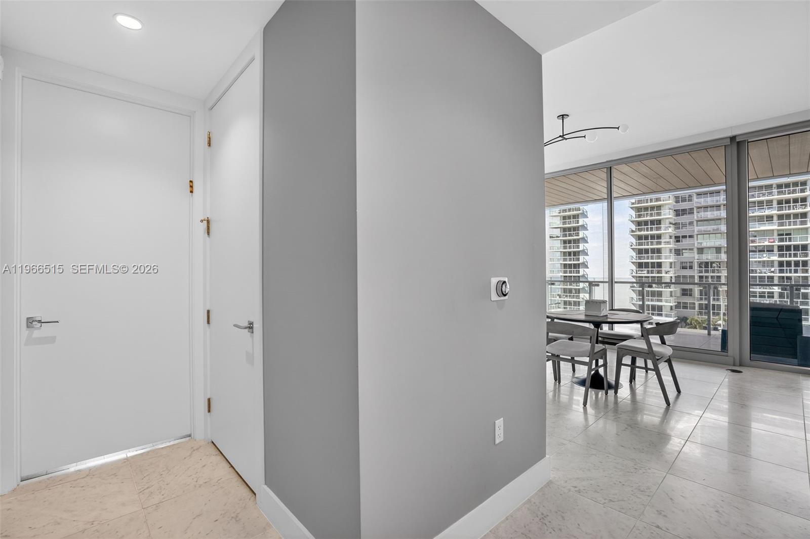 A gray wall separates a tiled entryway from a dining area with floor-to-ceiling windows — 5775 Collins Ave # 506, Miami Beach FL 33140, MIAMI BEACH, FL