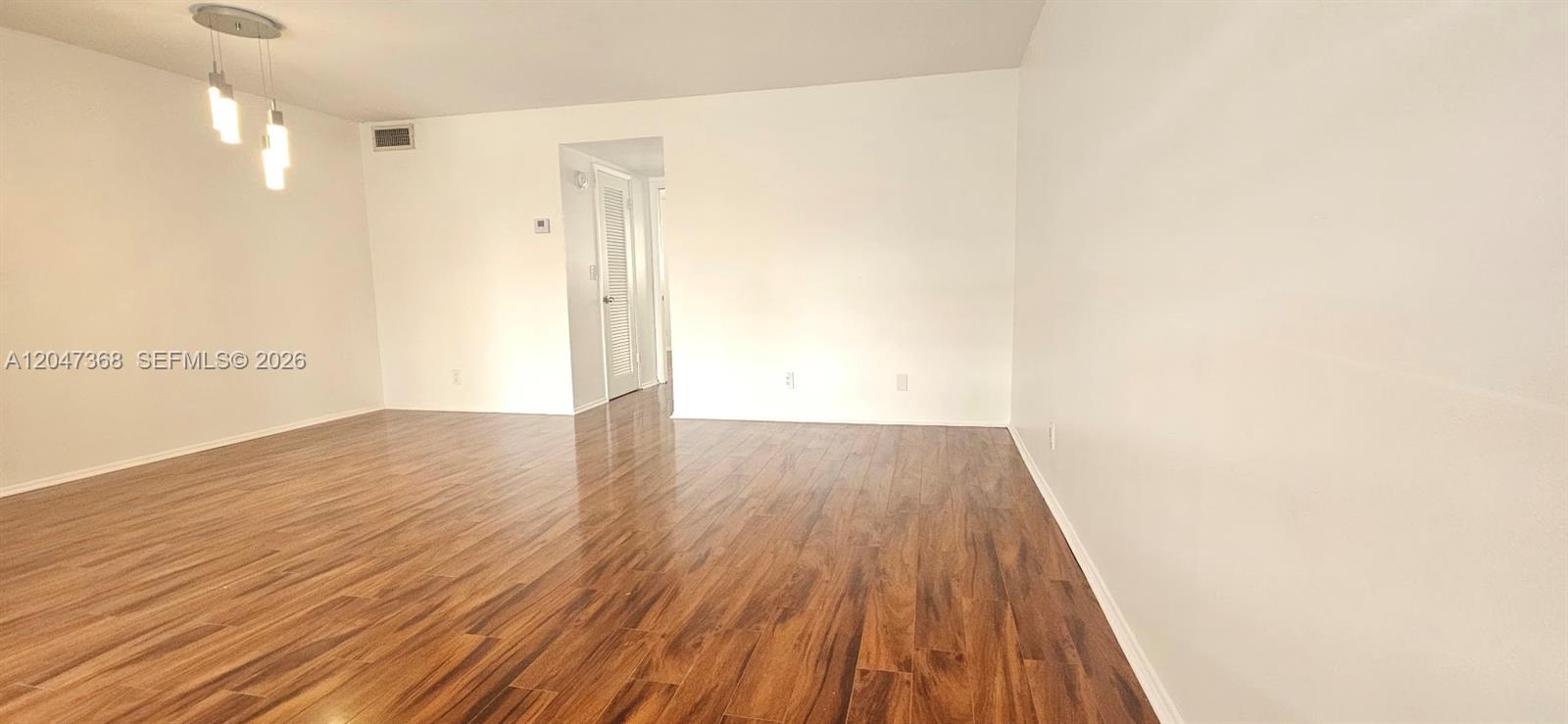 An empty room features light-colored walls, a wood-look floor, and a modern pendant light fixture — 300 Layne Blvd # 313, Hallandale Beach FL 33009, HALLANDALE BEACH, FL