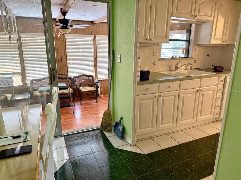 A kitchen with white cabinets and green walls opens to a sunroom with wicker furniture — 8144 RIDGE DALE AVENUE, BROOKSVILLE, FL