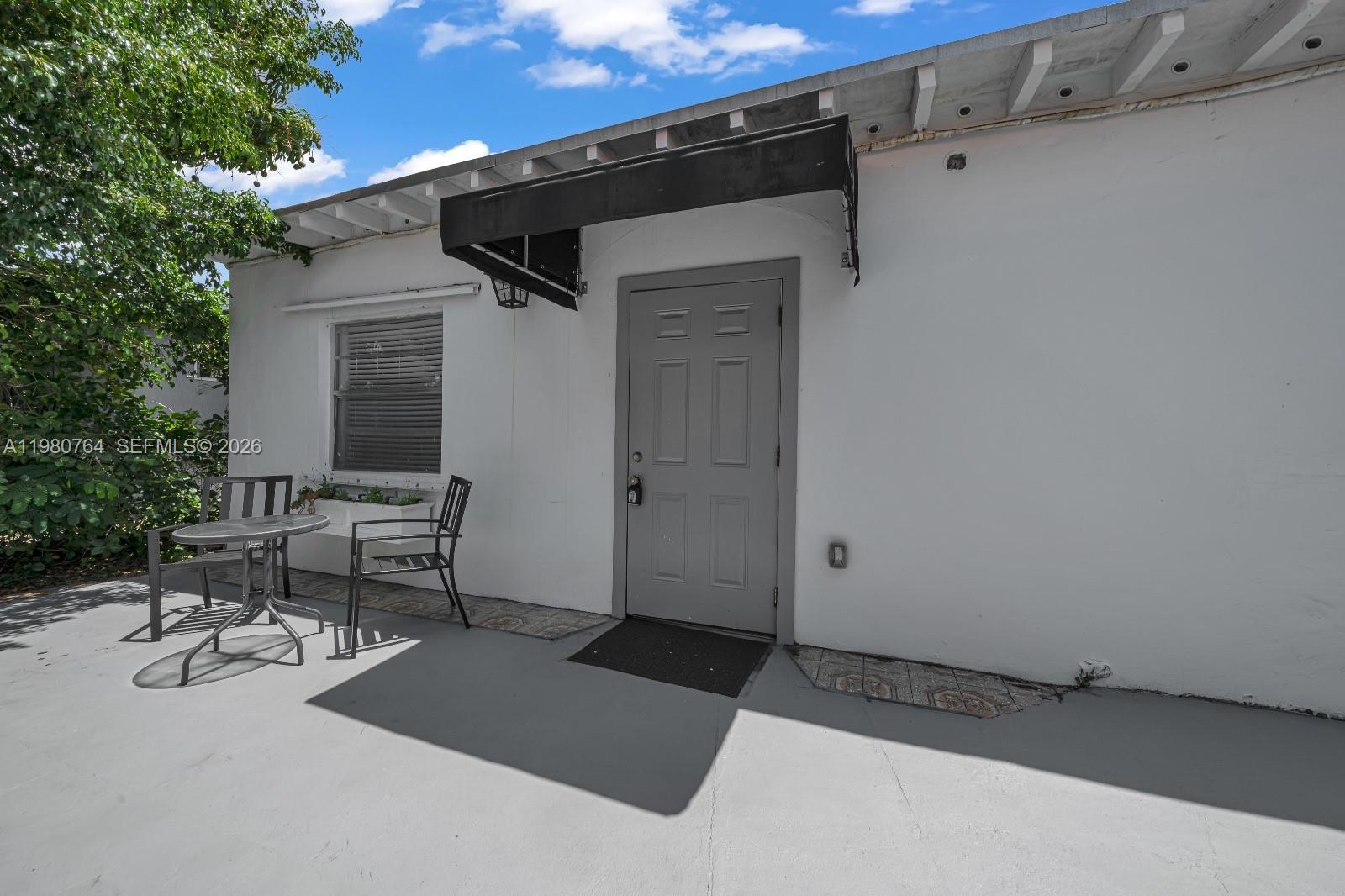 A gray door and a small patio table with chairs sit against a white wall — 1044 SW 13th Ct # 2, Miami FL 33135, MIAMI, FL