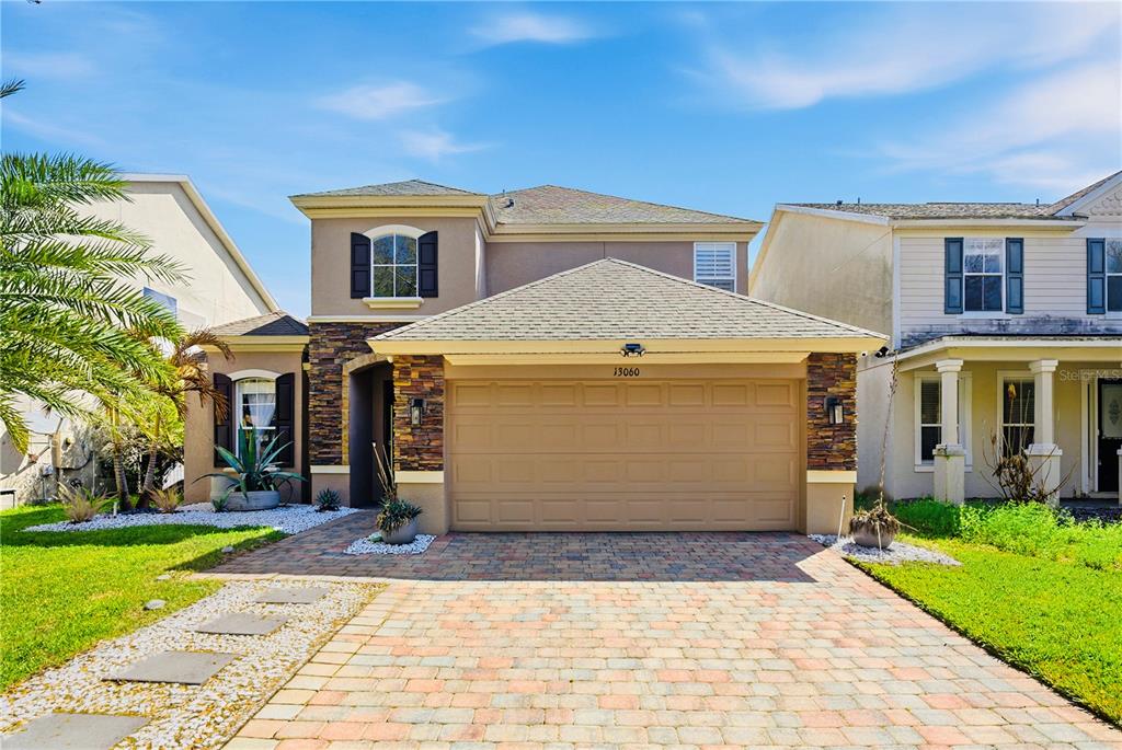 A two-story suburban house features a tan stucco exterior, stone accents, and a paved driveway — 13060 HATHERTON CIRCLE, ORLANDO, FL