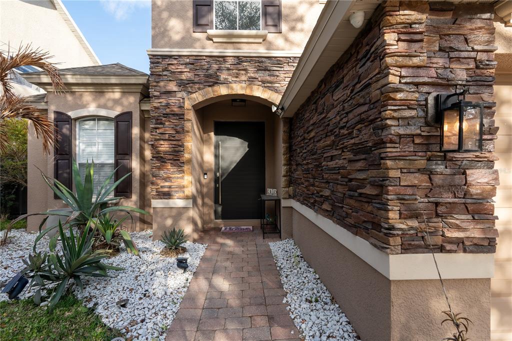 A stone-accented house exterior features a dark front door, a paver walkway, and desert landscaping — 13060 HATHERTON CIRCLE, ORLANDO, FL