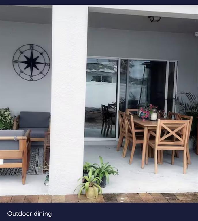 A covered patio features a wooden dining set, lounge chairs, and a metal compass wall decoration — 440 TISONE LANE, DAVENPORT, FL