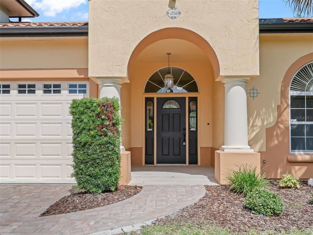 The exterior of a house features a tan stucco facade, a dark door, and columns — 1256 AVENIDA DE LAS CASAS, LADY LAKE, FL