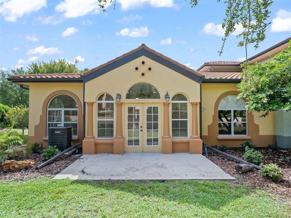 The exterior of a house features a tan stucco facade, arched windows, and French doors — 1256 AVENIDA DE LAS CASAS, LADY LAKE, FL