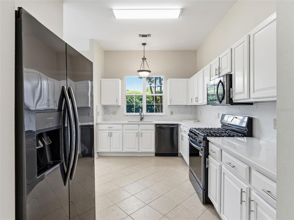 A kitchen features white cabinets, black appliances, light countertops, and a window above the sink — 1256 AVENIDA DE LAS CASAS, LADY LAKE, FL