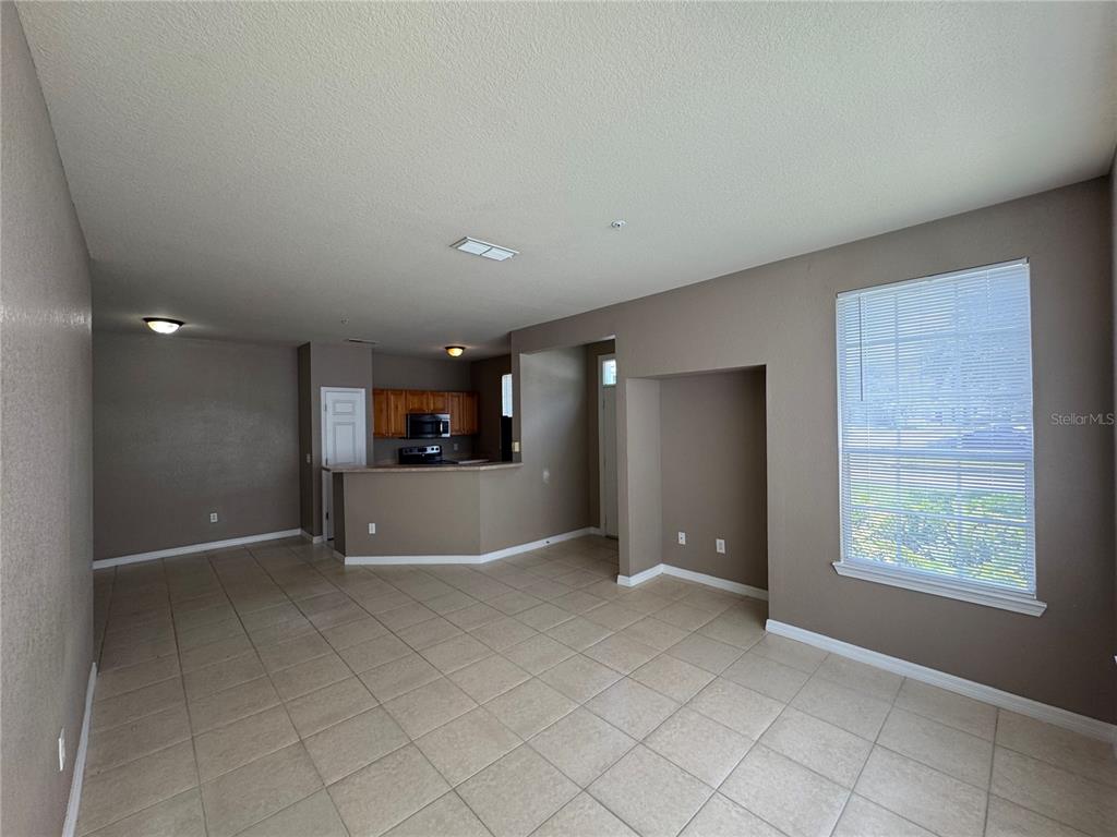 An open-concept living area features tan tile flooring, brown walls, and a kitchen with wooden cabinets — 9061 LEE VISTA BOULEVARD UNIT 1306, ORLANDO, FL