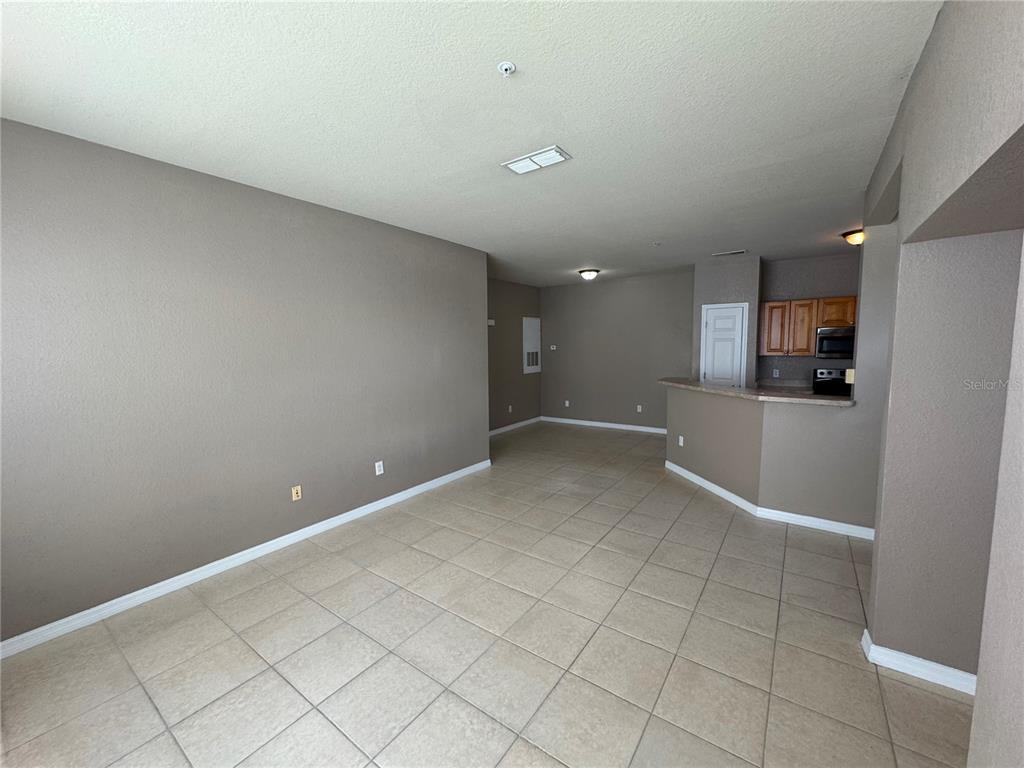An open-concept living area features beige tile flooring, neutral walls, and a kitchen breakfast bar — 9061 LEE VISTA BOULEVARD UNIT 1306, ORLANDO, FL