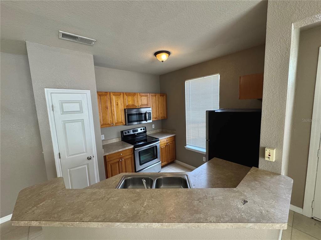 A kitchen features wood cabinets, stainless steel appliances, a double sink, and laminate countertops — 9061 LEE VISTA BOULEVARD UNIT 1306, ORLANDO, FL
