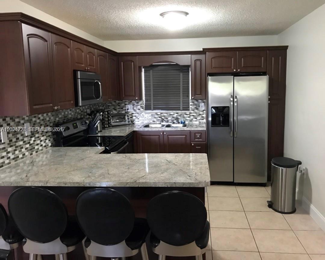 A kitchen features dark wood cabinets, granite countertops, stainless steel appliances, and a tiled backsplash — 15302 SW 180th Ter, Miami FL 33187, MIAMI, FL