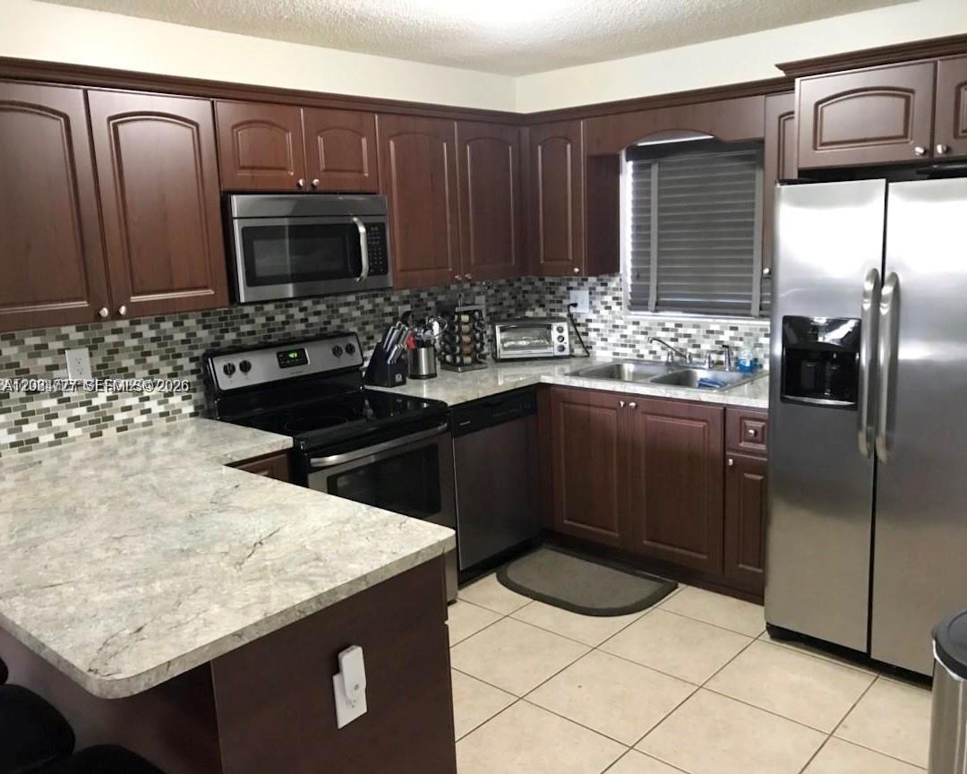 A kitchen features dark wood cabinets, stainless steel appliances, and a light-colored stone countertop — 15302 SW 180th Ter, Miami FL 33187, MIAMI, FL