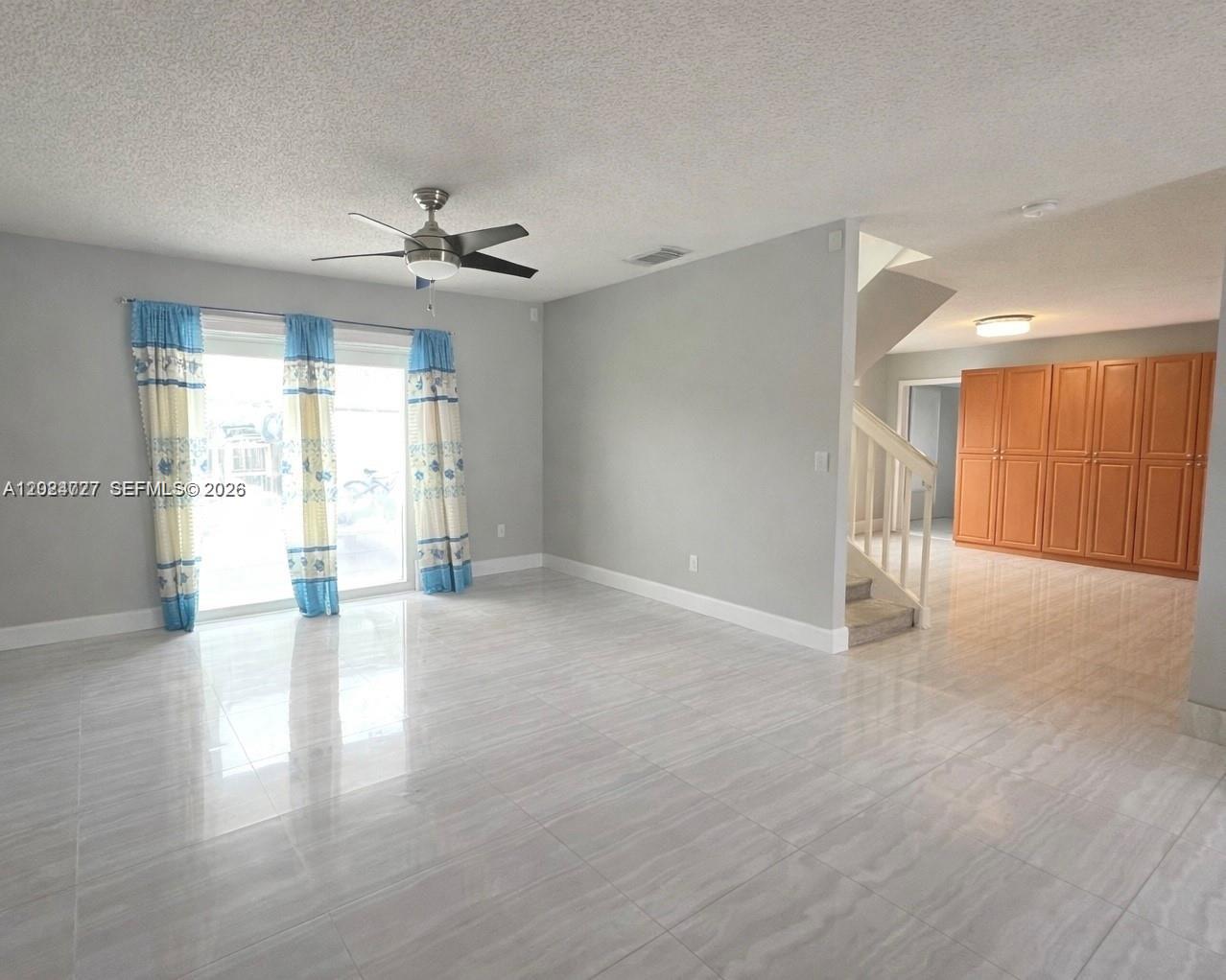 A living room with light gray walls, large tile flooring, a ceiling fan, and stairs — 15302 SW 180th Ter, Miami FL 33187, MIAMI, FL