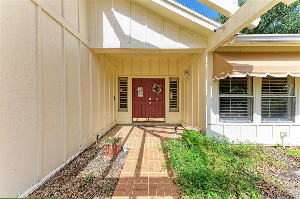 A red double front door is centered at the end of a tiled walkway — 1003 83RD STREET NW, BRADENTON, FL