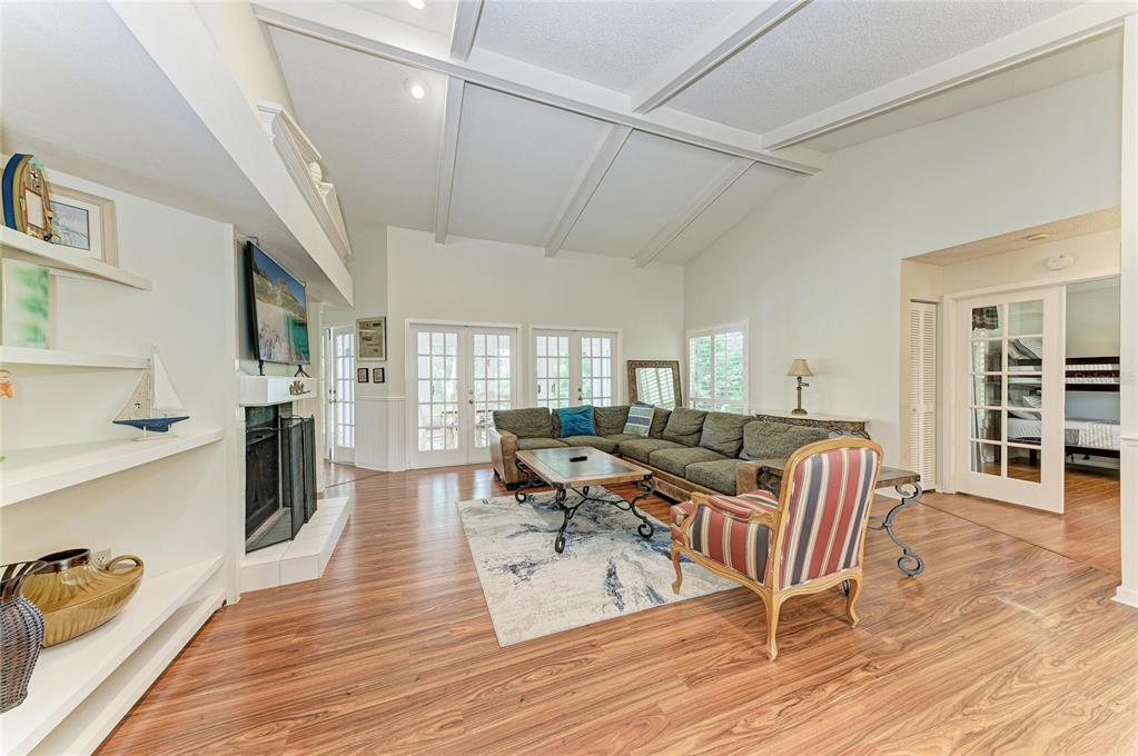 A living room features a vaulted ceiling, fireplace, sectional sofa, and wood-look flooring — 1003 83RD STREET NW, BRADENTON, FL