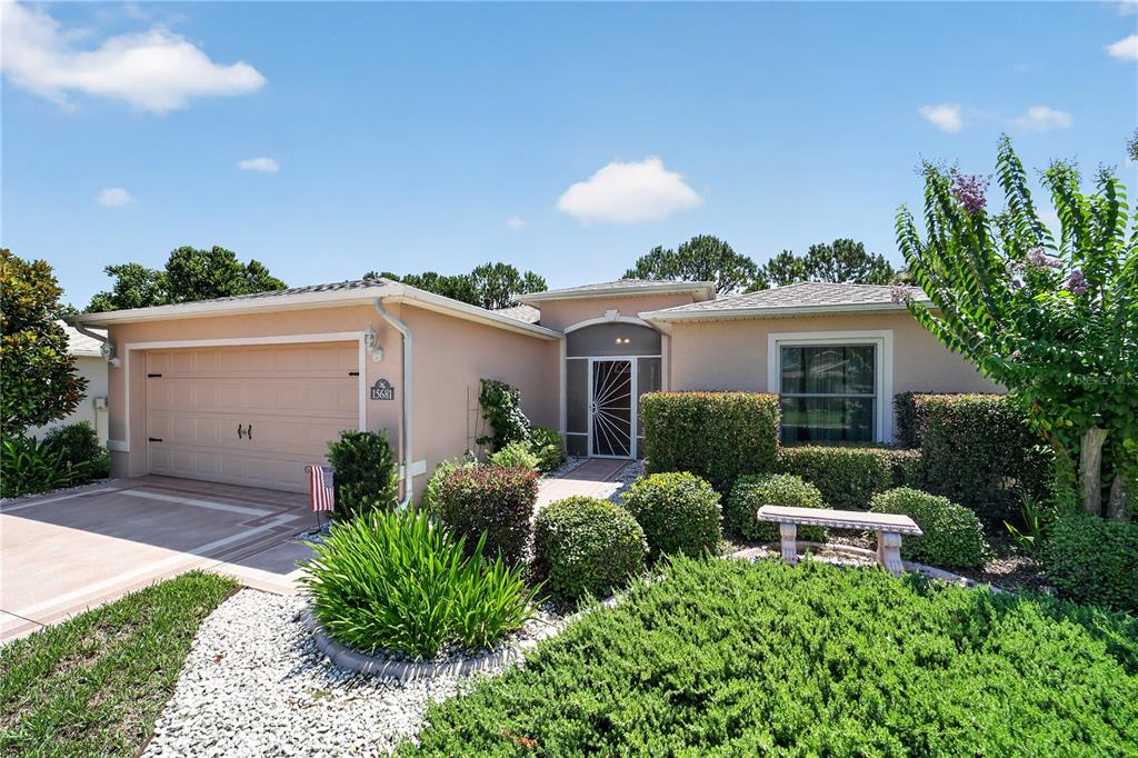A single-story house with a beige stucco exterior, a two-car garage, and landscaped front yard — 15681 SW 14TH AVENUE ROAD, OCALA, FL