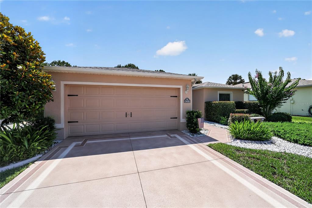 A tan single-story house features a two-car garage, a concrete driveway, and landscaped front yard — 15681 SW 14TH AVENUE ROAD, OCALA, FL