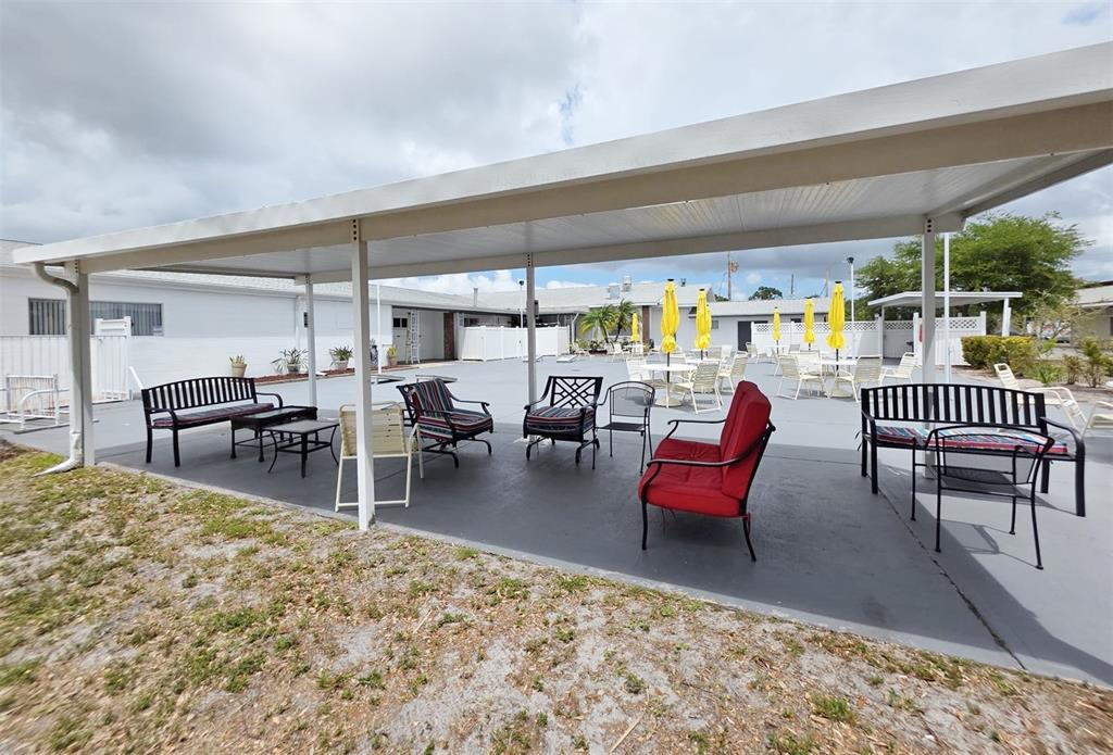 A covered outdoor patio features various seating arrangements, including benches and chairs, on a concrete surface — 6015 19TH STREET N UNIT 314, ST PETERSBURG, FL