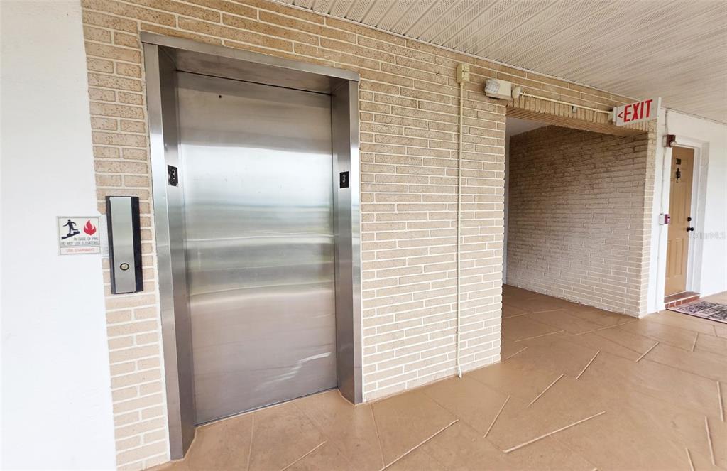 A stainless steel elevator door is set into a light-colored brick wall in a hallway — 6015 19TH STREET N UNIT 314, ST PETERSBURG, FL