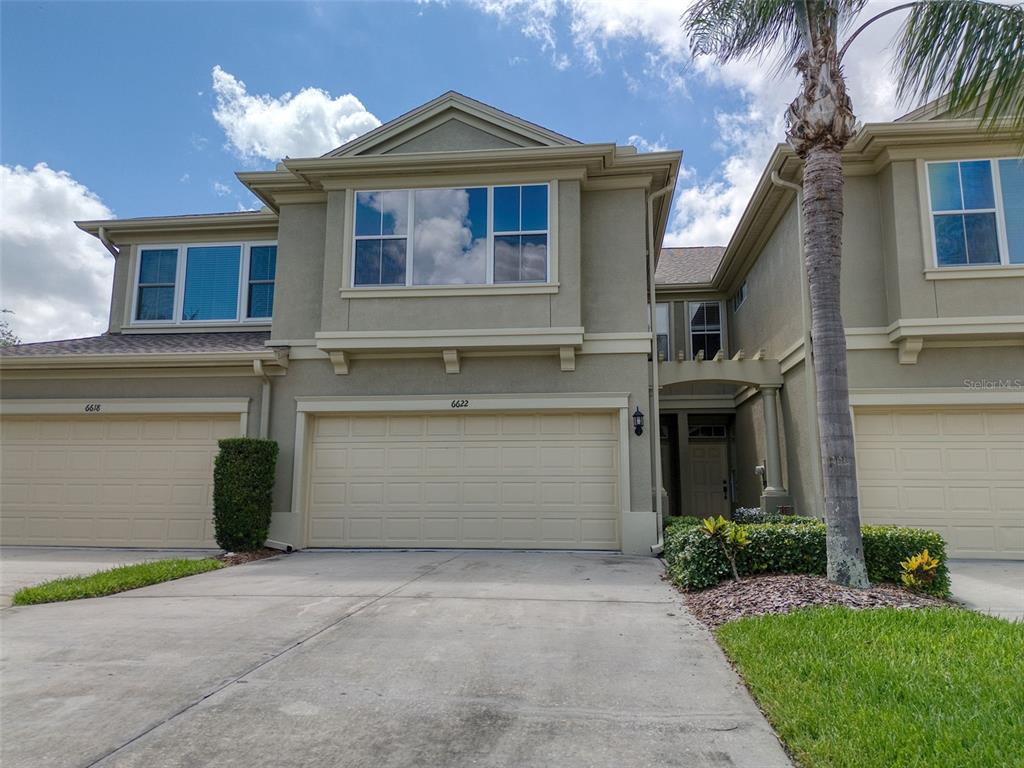 The exterior of a two-story townhouse features a beige stucco facade and a double garage — 6622 83RD AVENUE N, PINELLAS PARK, FL