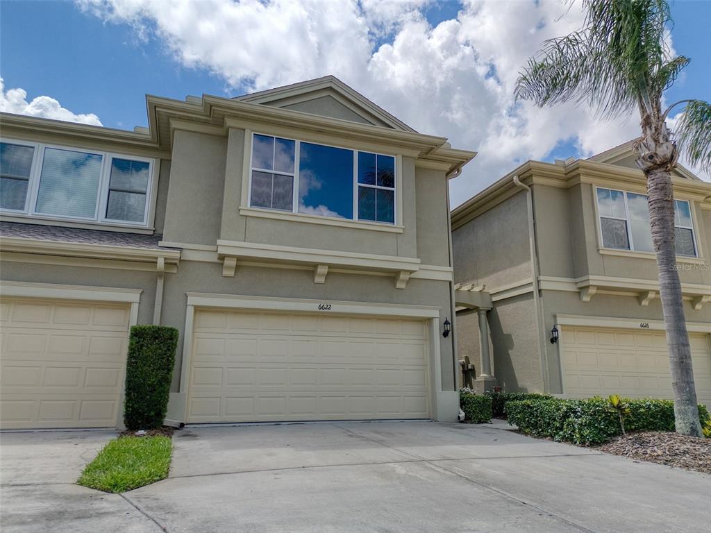 A two-story townhouse exterior features a beige stucco facade, a two-car garage, and a palm tree — 6622 83RD AVENUE N, PINELLAS PARK, FL