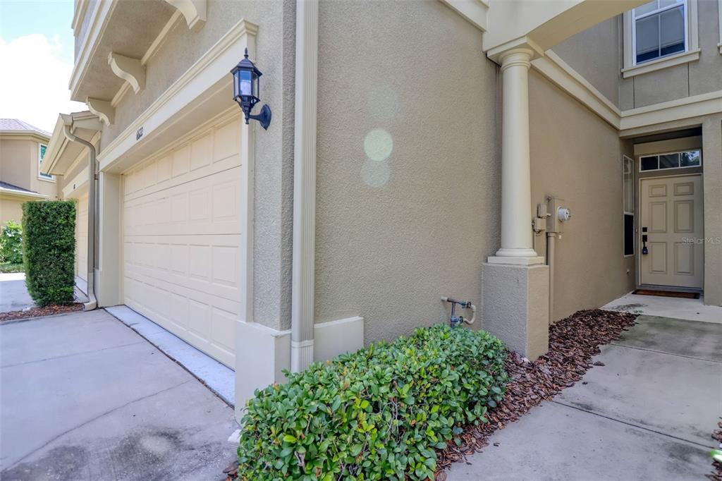 A beige house exterior features a garage, a front door, and a small landscaped bush — 6622 83RD AVENUE N, PINELLAS PARK, FL
